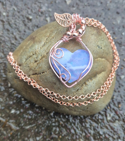 A heart shaped purple stone with cloud like patterns wrapped in whorls and swirls of rose gold coloured wire